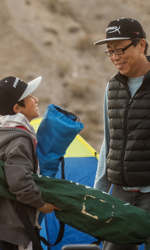A father and son smile at each other in front of a tent