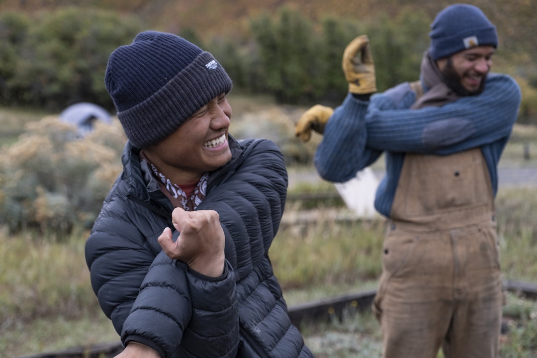 Two people, dressed in layers of clothing, stretch their arms and smile