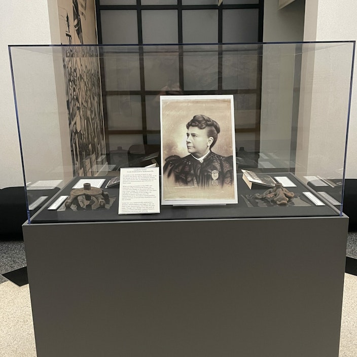 A glass case houses a black and white image of a woman, plus small items