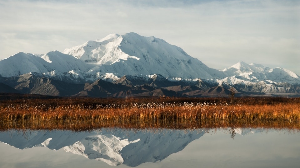 A still lake reflects a snowy mountain and an autumnal landscape
