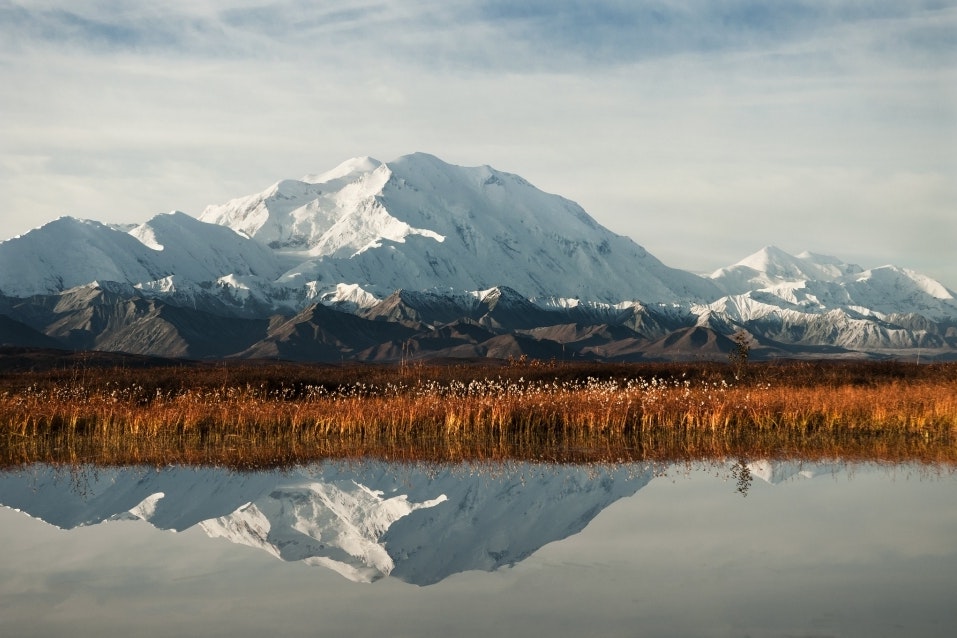 A still lake reflects a snowy mountain and an autumnal landscape