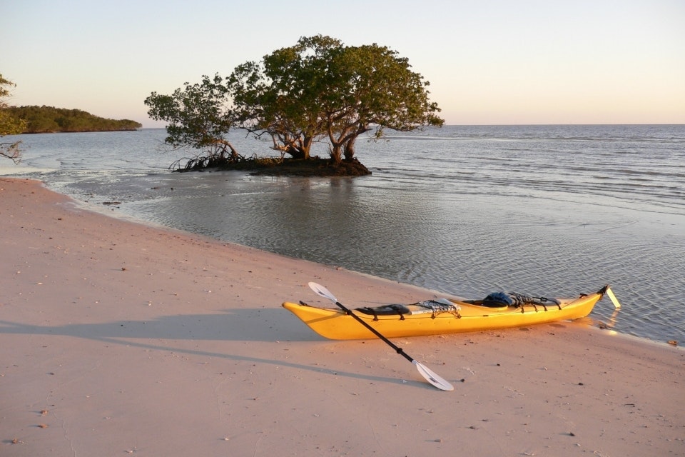 A yellow canoe in sand in front of a shoreline