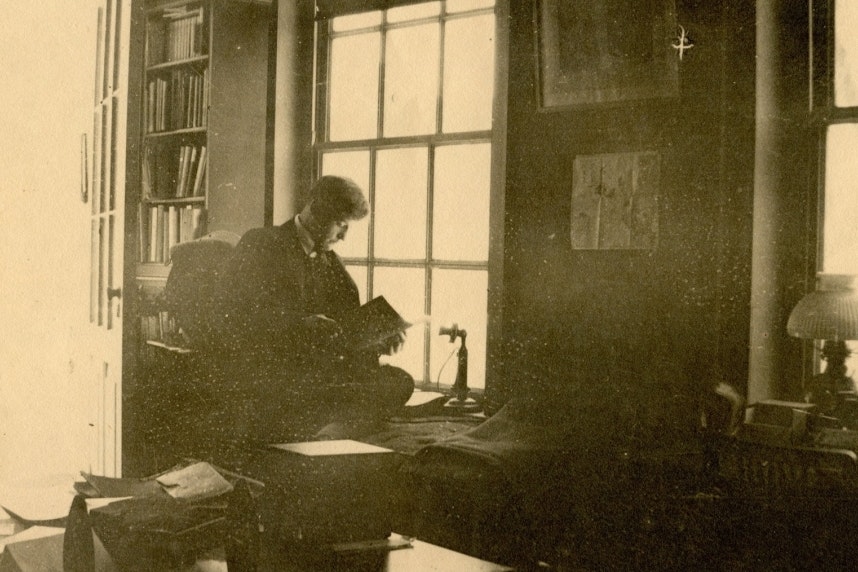 Historic photo of a person sitting in a library and reading by a window