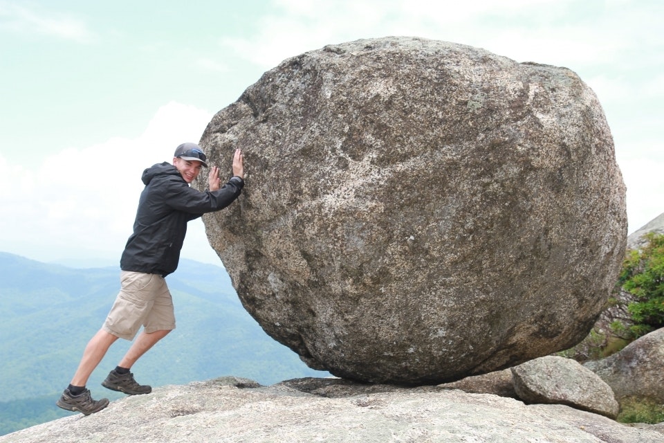 Man pretending to push a giant boulder bigger than he is at Old Rag hike in Shenandoah National Park