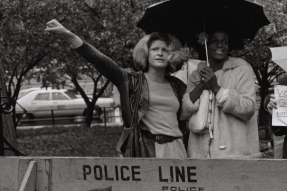 Historic photo of two people standing at a picket line, crowding under an umbrella