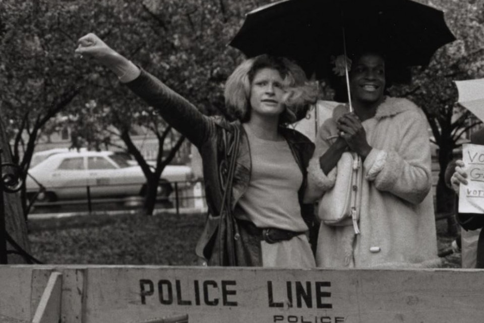 Historic photo of two people standing at a picket line, crowding under an umbrella