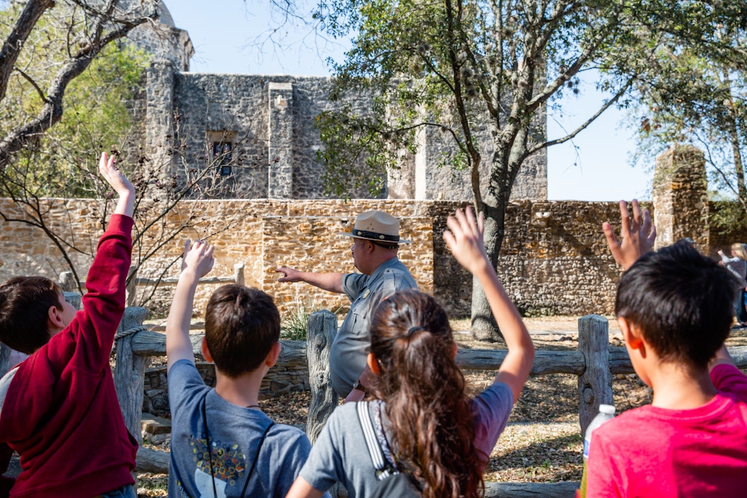 A group of kids raise their hands in front of a historic mission