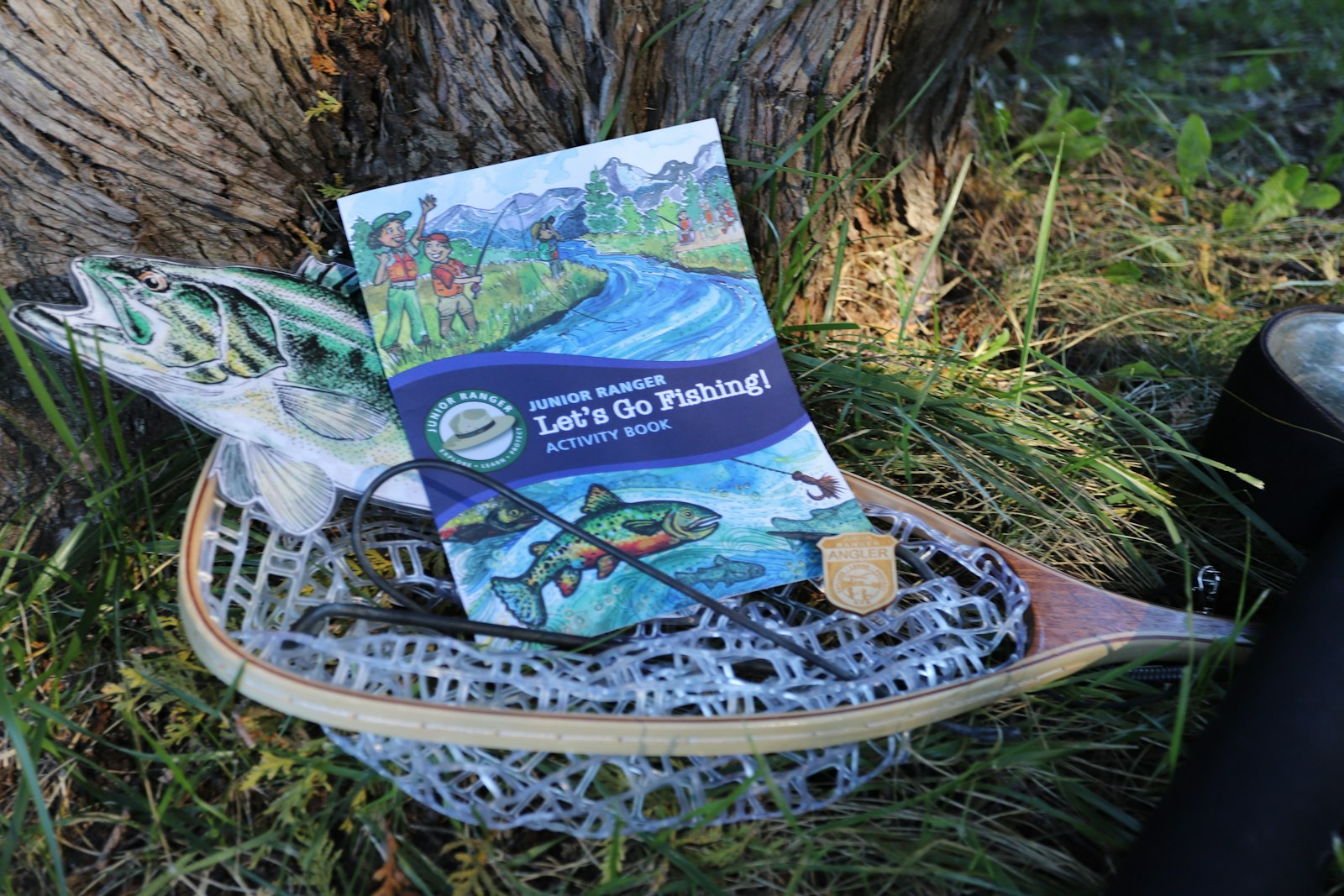 A booklet in a fishing basket. The booklet text reads: "Junior Ranger Let's Go Fishing Activity Book"