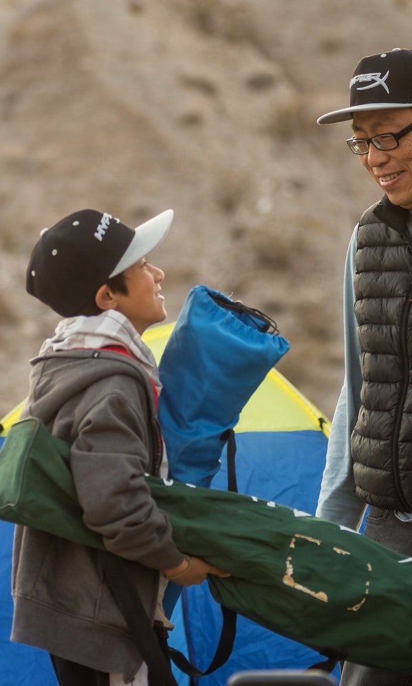 A father and son smile at each other in front of a tent
