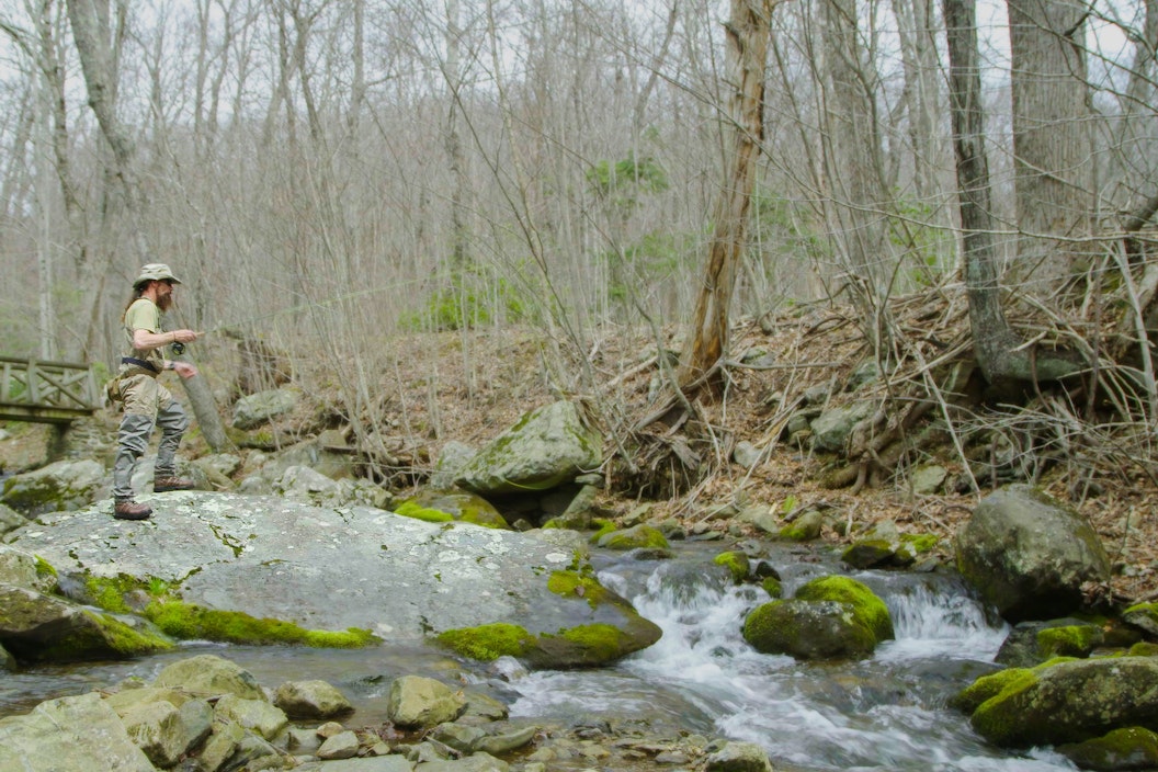 A person fly fishes along a rocky stream