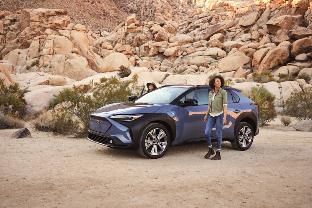 Two people stand outside of a blue car, parked within a desert landscape