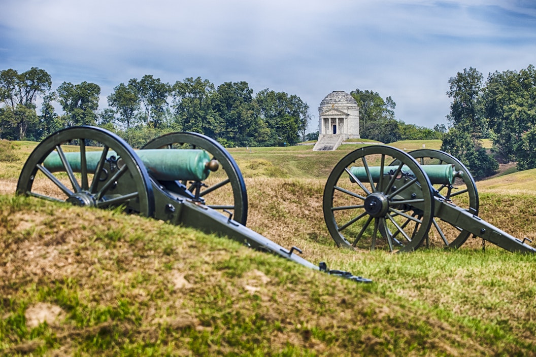 Two historic cannons lie in the foreground. In the background, a white stone memorial