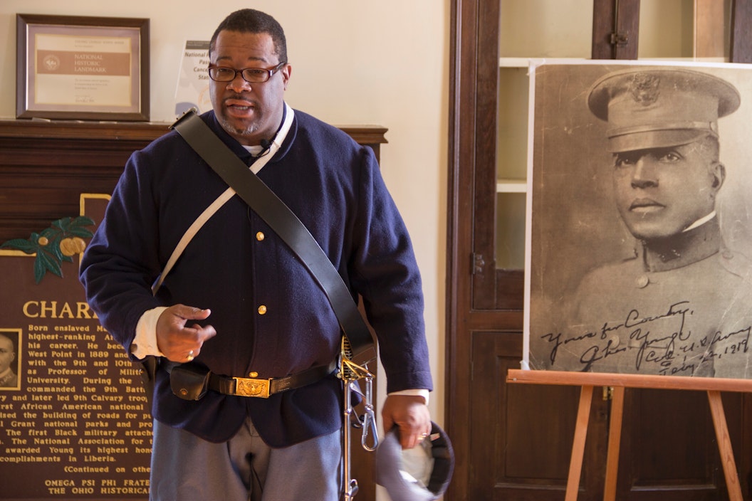 Ranger dressed in a military uniform gives a speech in front of a historic photo of Charles Young