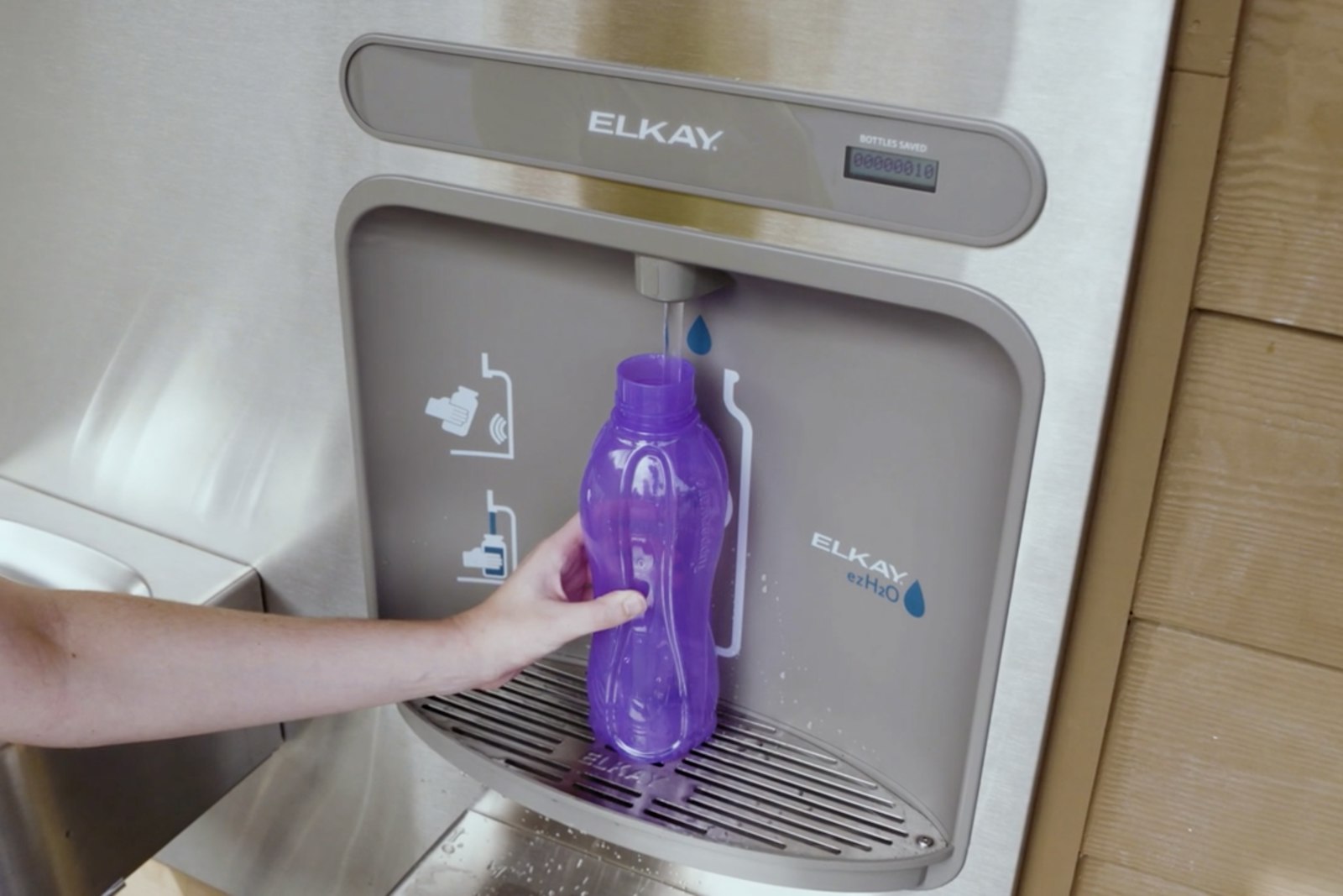 Hand holding Tupperware water bottle, refilling at fountain refill station