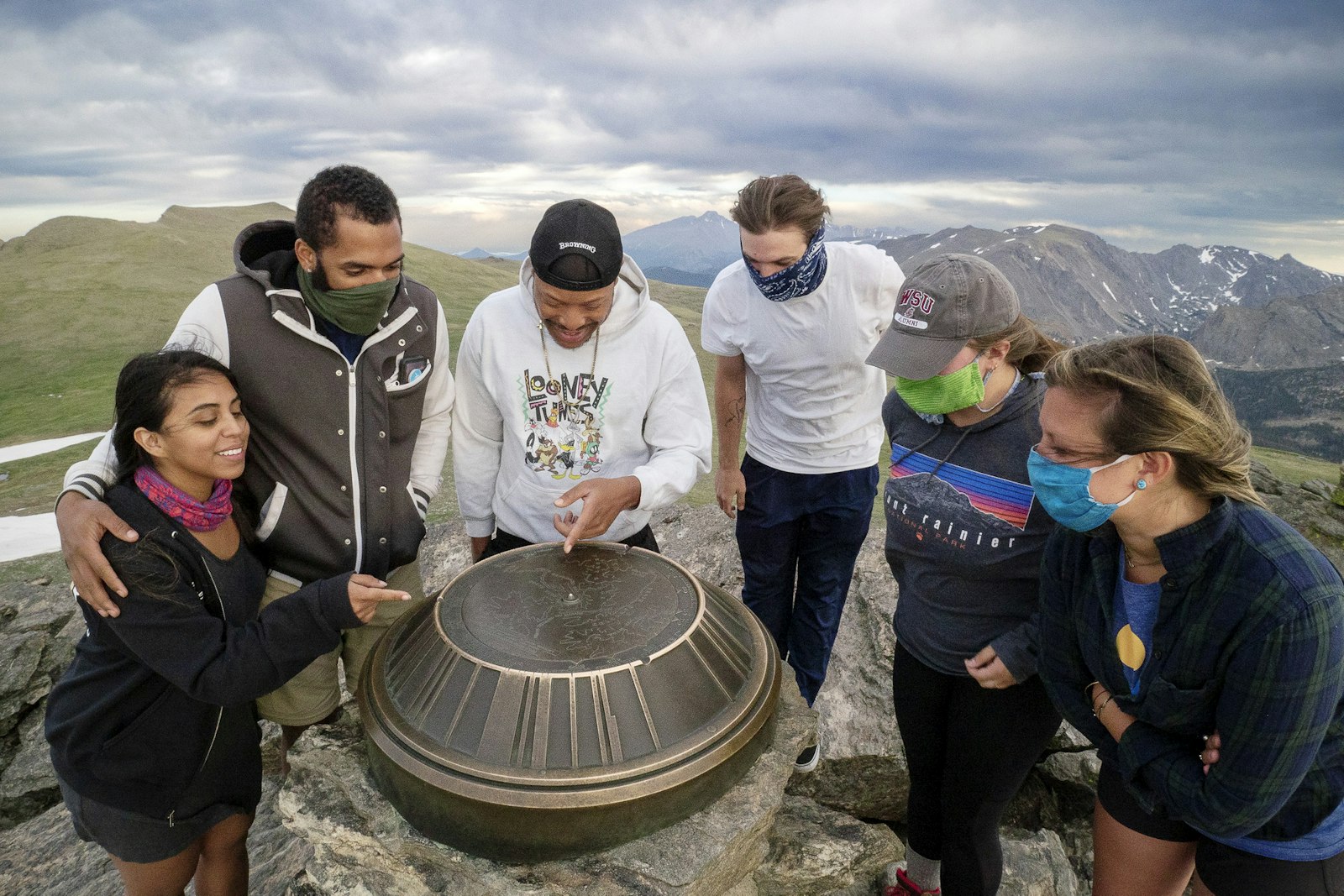 A group of people lean towards an index at the summit of a mountain