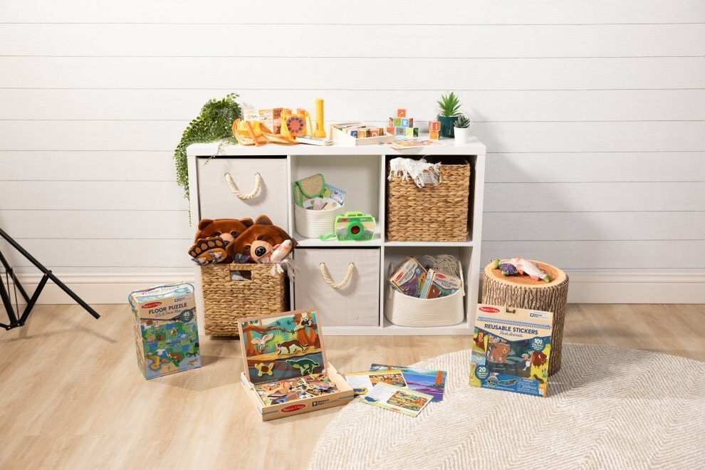 A storage container with 6 removable cubes sits against a wall. Around and inside it is a collection of national park inspired toys