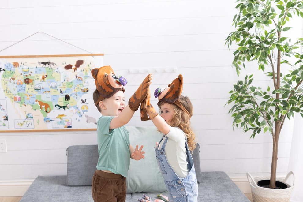 Two children wear headbands with bear faces on them, and a mitten that looks like a bear paw. They high-five