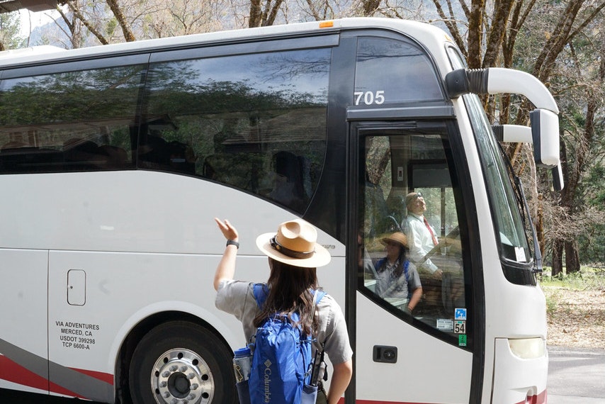 A park ranger waves goodbye to a bus filled with students