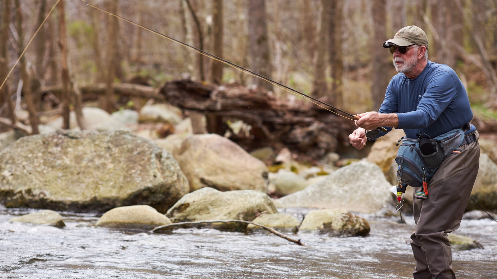 A person goes fly fishing in a stream that reaches up to his knees