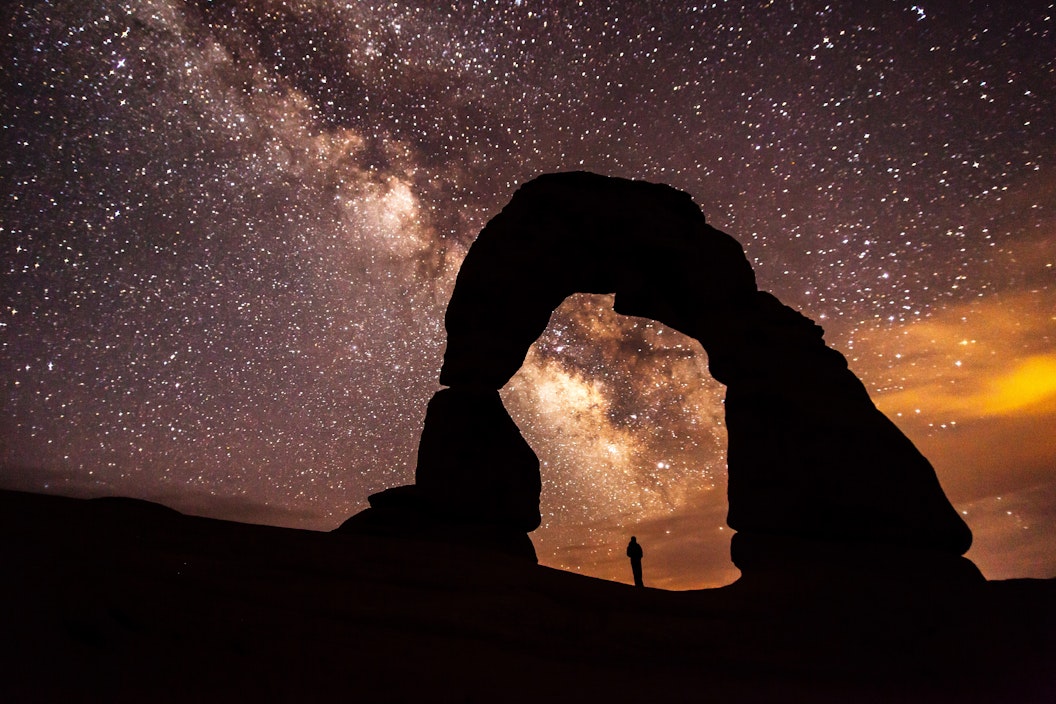 A person walks under an arch; they're silhouetted against a starry sky
