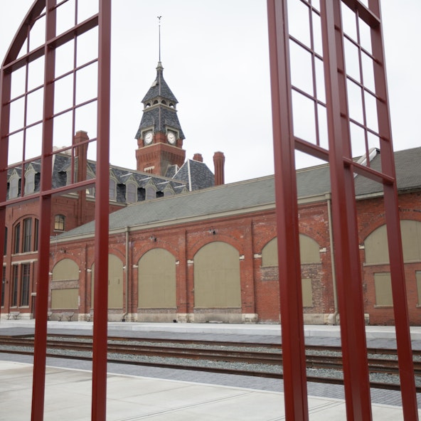 A red metal fence opens to a historic red brick building with a clock tower