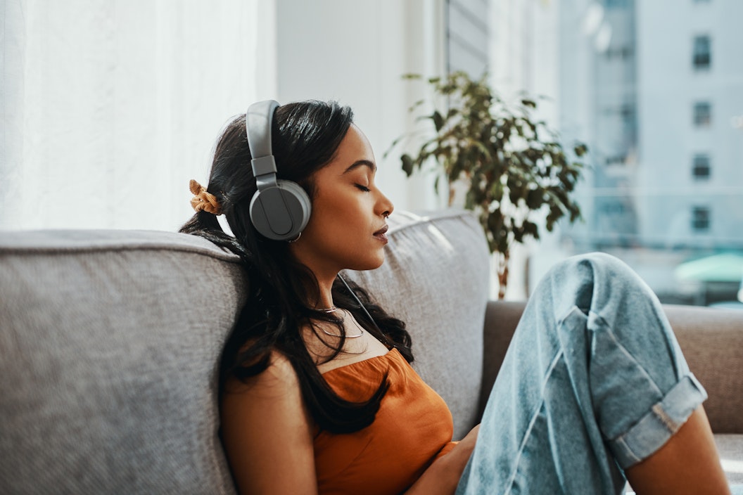 A person sits on a couch, they're wearing headphones and have their eyes closed