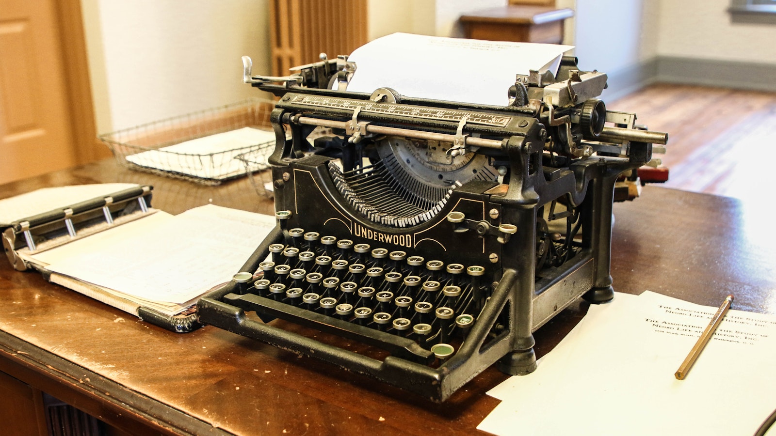 Vintage typewriter and sheets of paper sit on a large wooden desk.