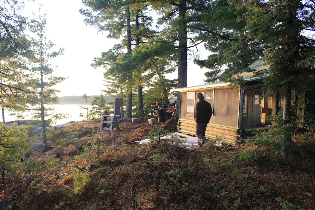 A group of people surround a small cabin on the shore of lake