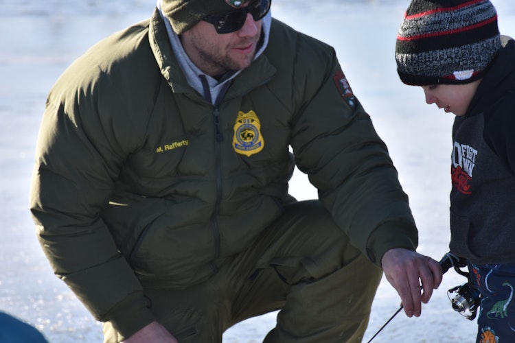 A park ranger teaching a boy how to ice fish