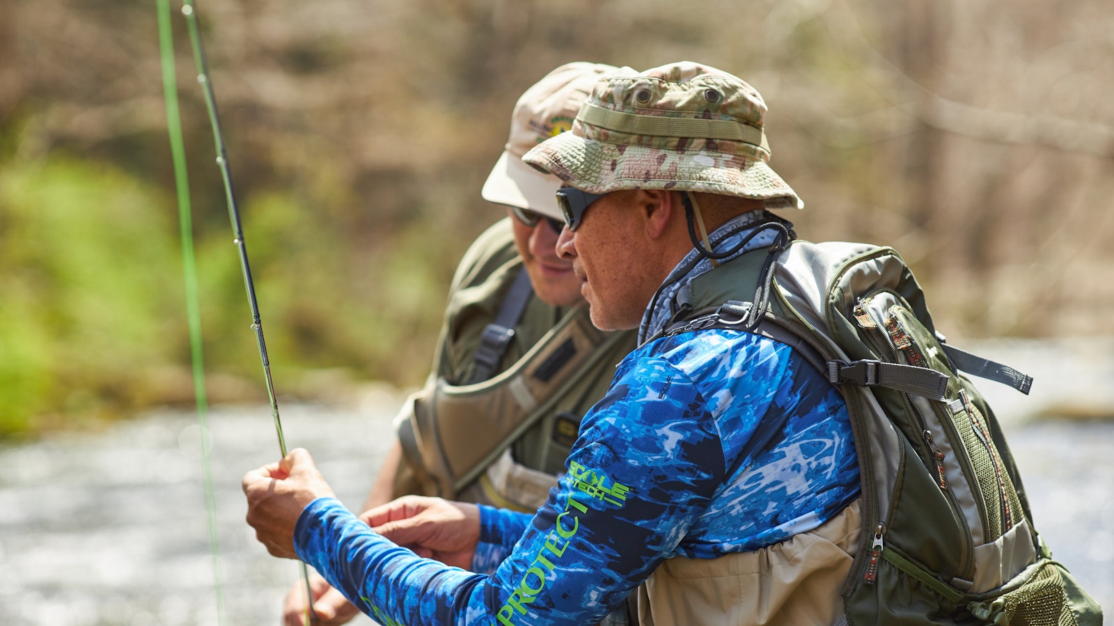 Two people lean toward each other to examine a fly fishing rod