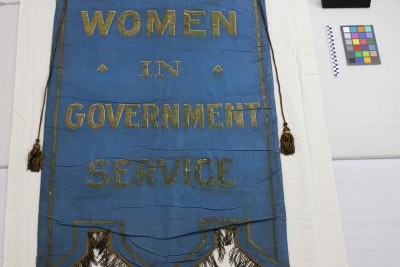 Archival photo of a blue banner that reads "Women in Government Service" on a white backdrop