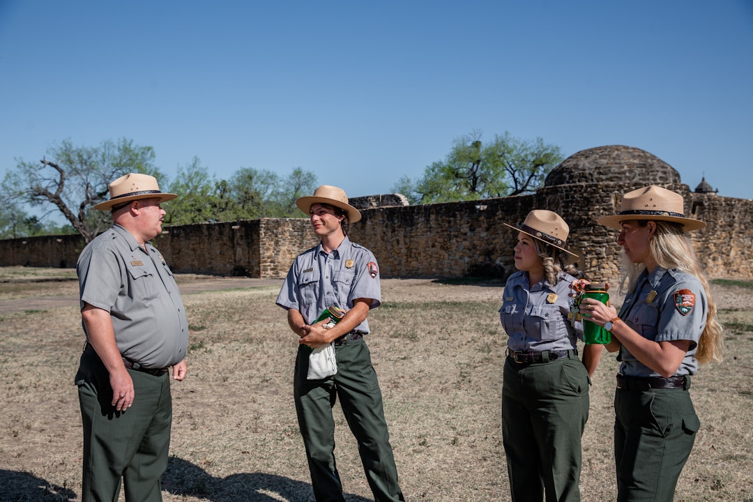 Four rangers, in uniform, stand and talk with each other