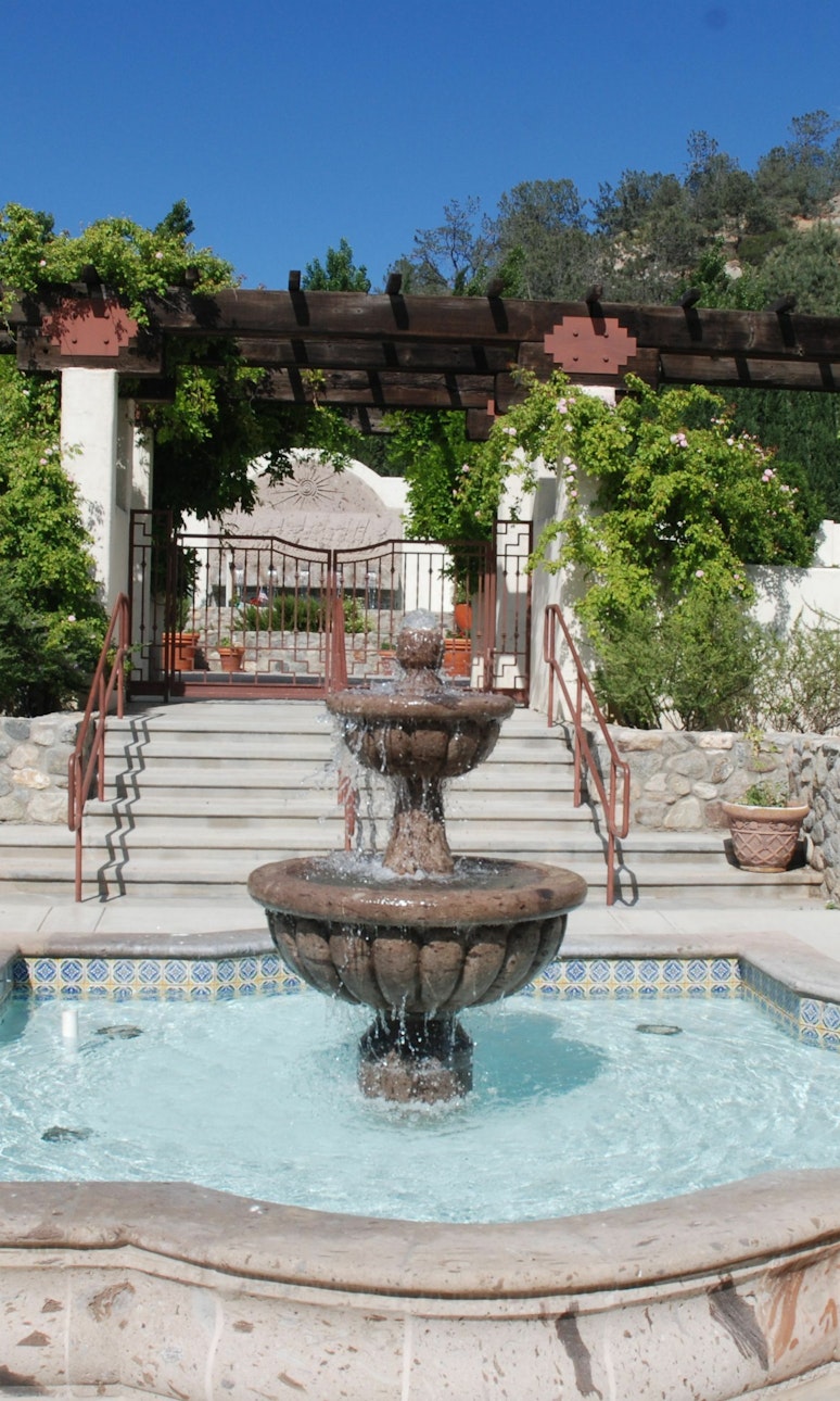A two-tiered fountain in front of a set of stairs that go up to an arbor.