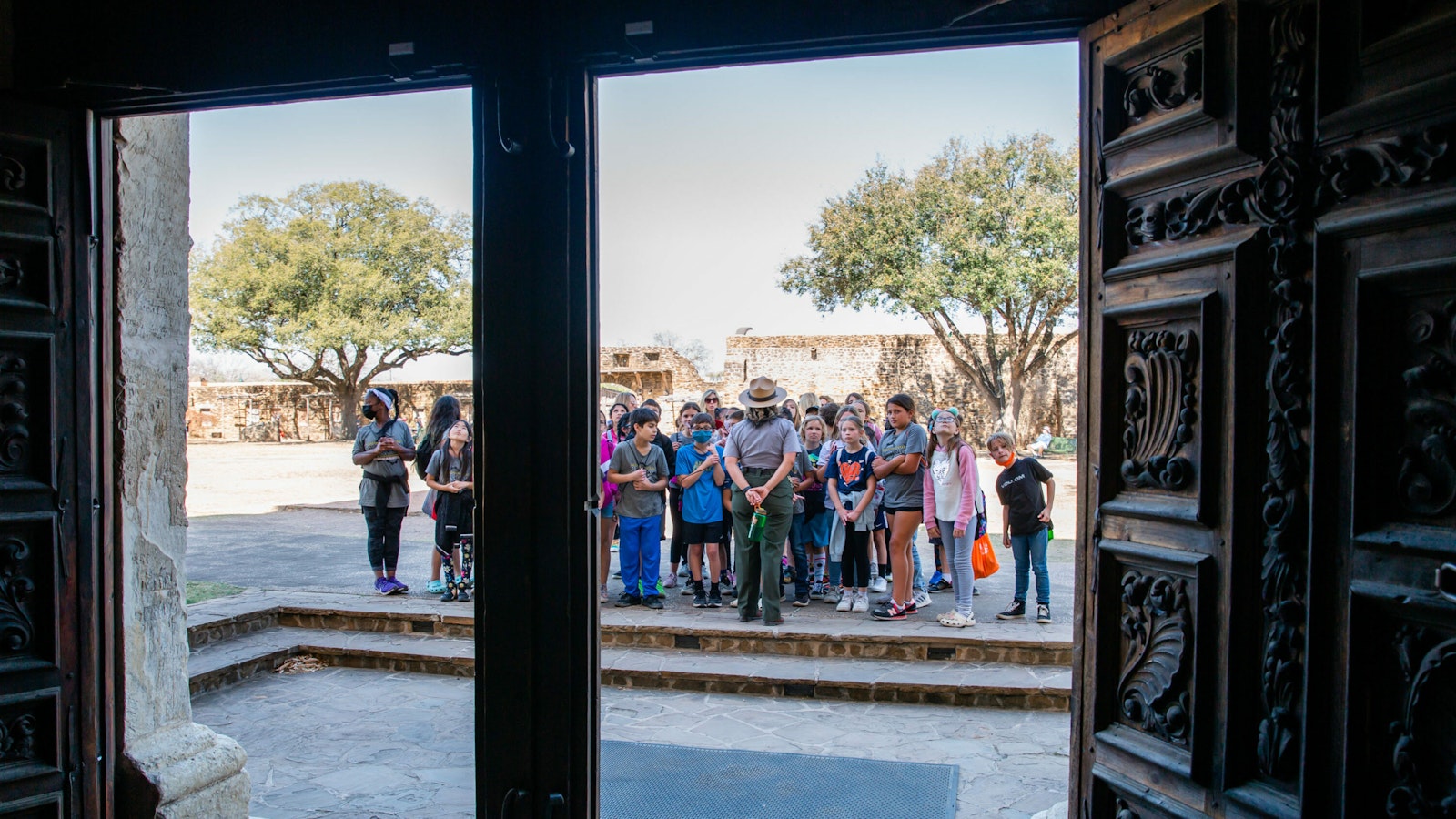 Through a set of historic, carved wooden doors, a group of students and a park ranger standing