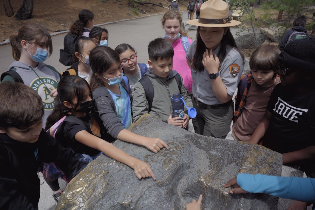 A group of students and uniformed ranger gather around to touch water pooling on a rock
