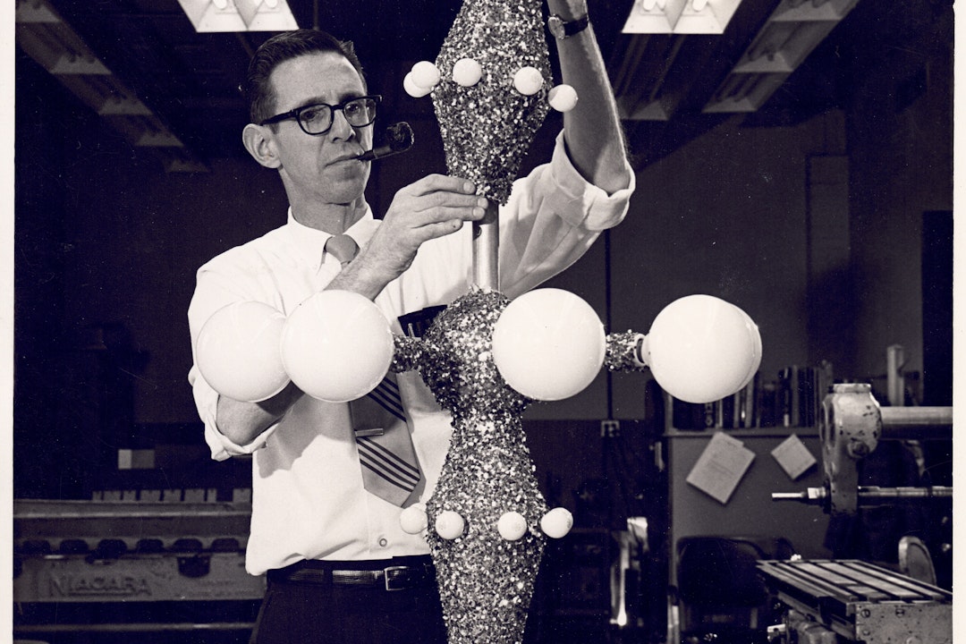A historic photo of a person fiddling with a tree topper. He wears glasses and smokes a pipe