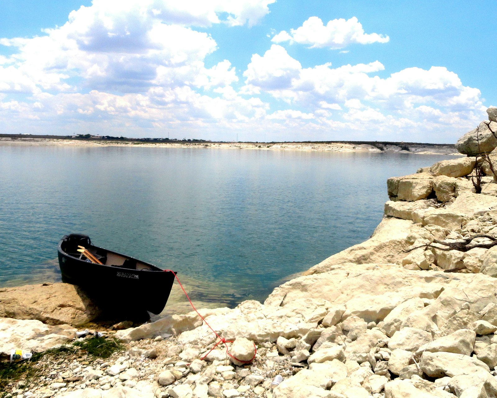 Dark-colored canoe beached on rocky outcropping with lake in background