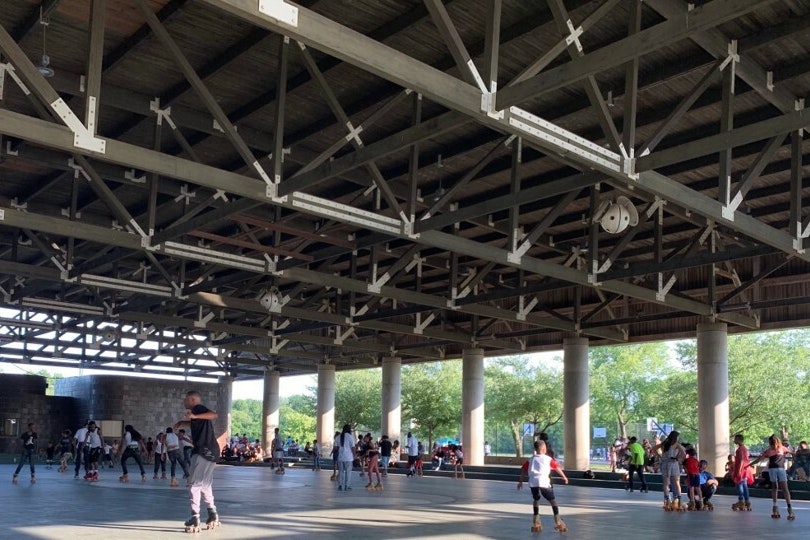 Covered roller skating pavilion with dozens of people roller skating and watching from bleachers on the side