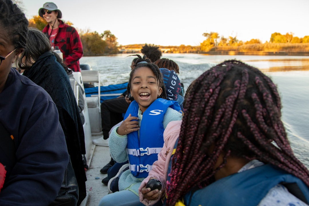 A young girl looks at her friend and laughs after being splashed with water during a boat tour