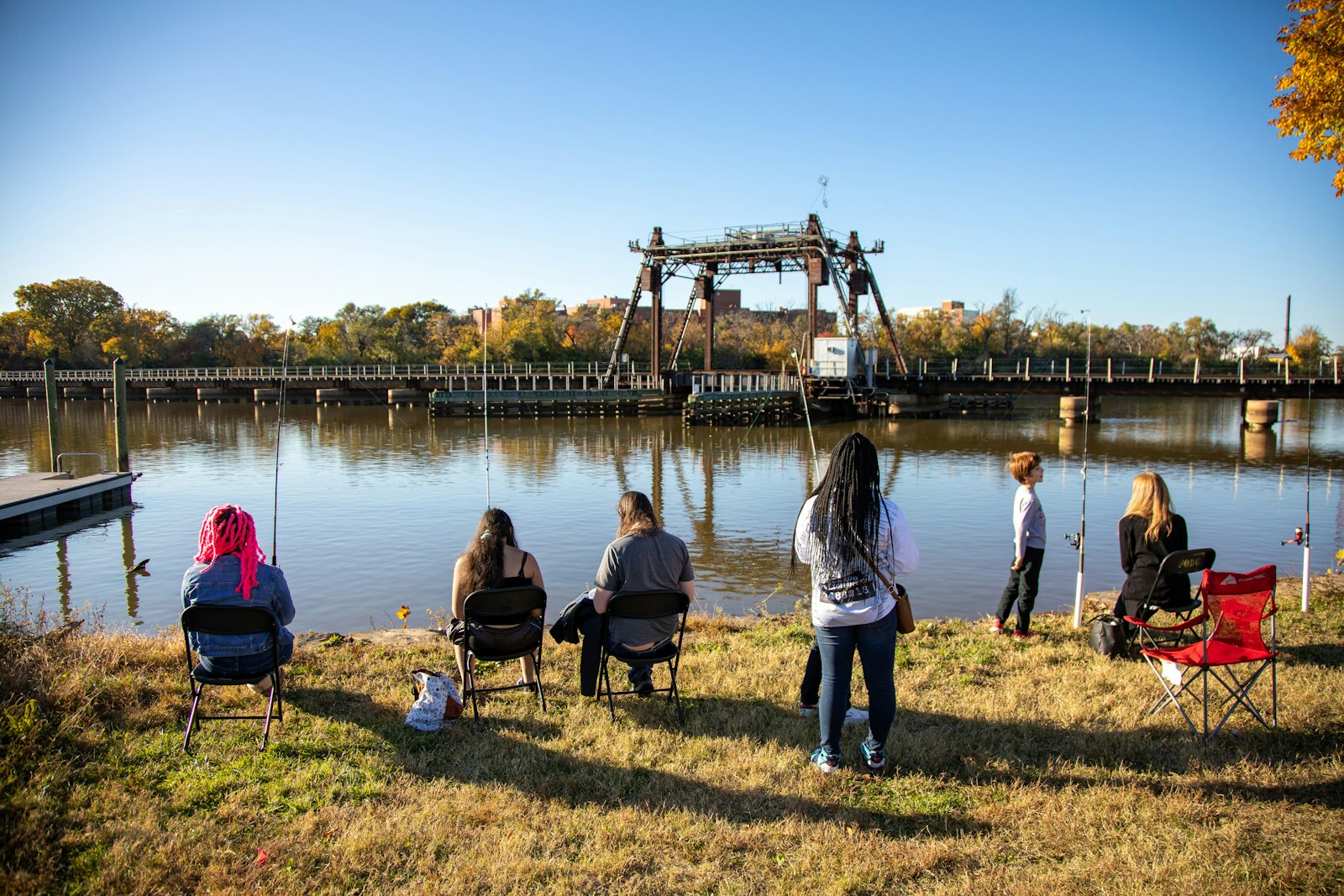 Six young people sit in chairs as they fish along the bank of the Anacostia River