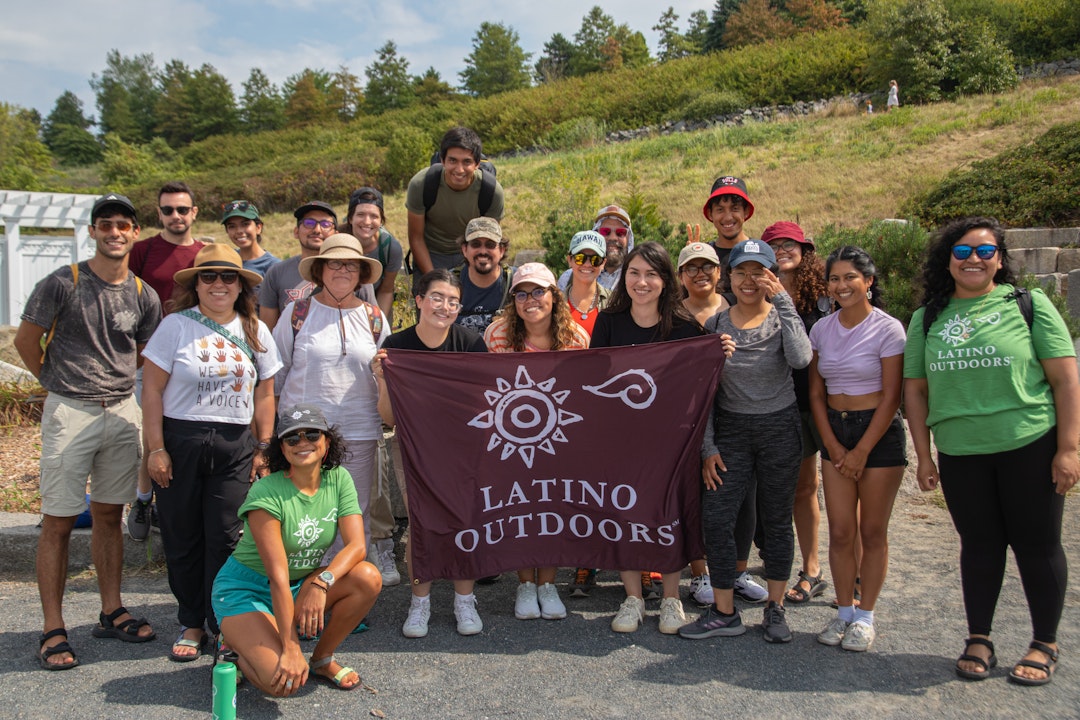 A group poses for a group photo. In the center, a few hold up a brown banner that reads "Latino Outdoors"