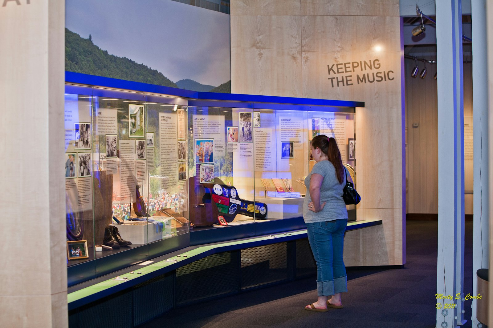 A person stands and looks at an exhibit about music behind glass