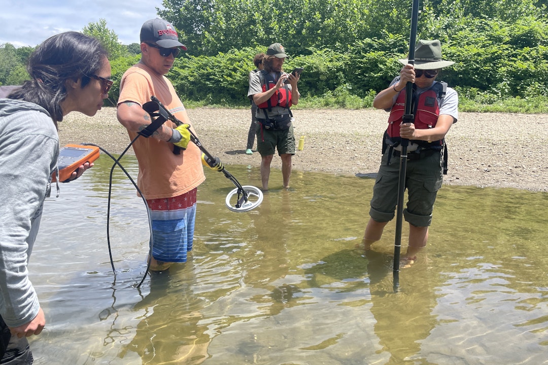 A group of people standing in a river with instruments to help track mussels.