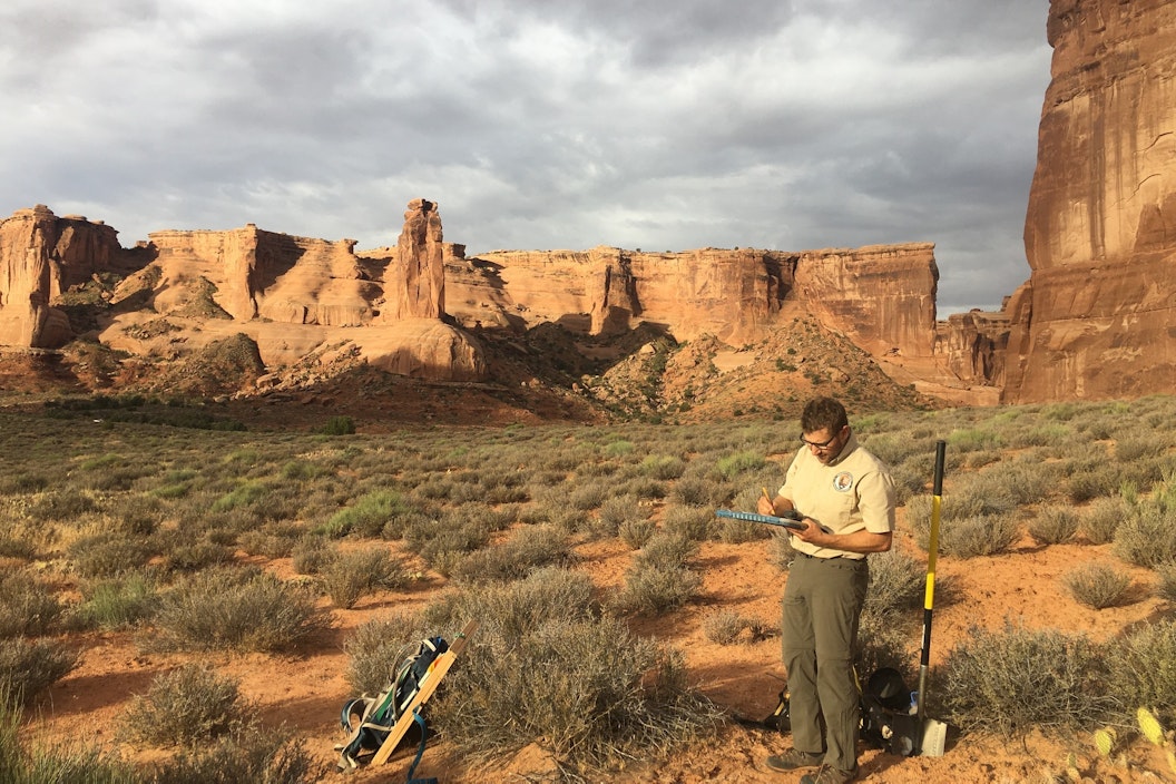 Person standing in desert canyon recording data on a field tablet