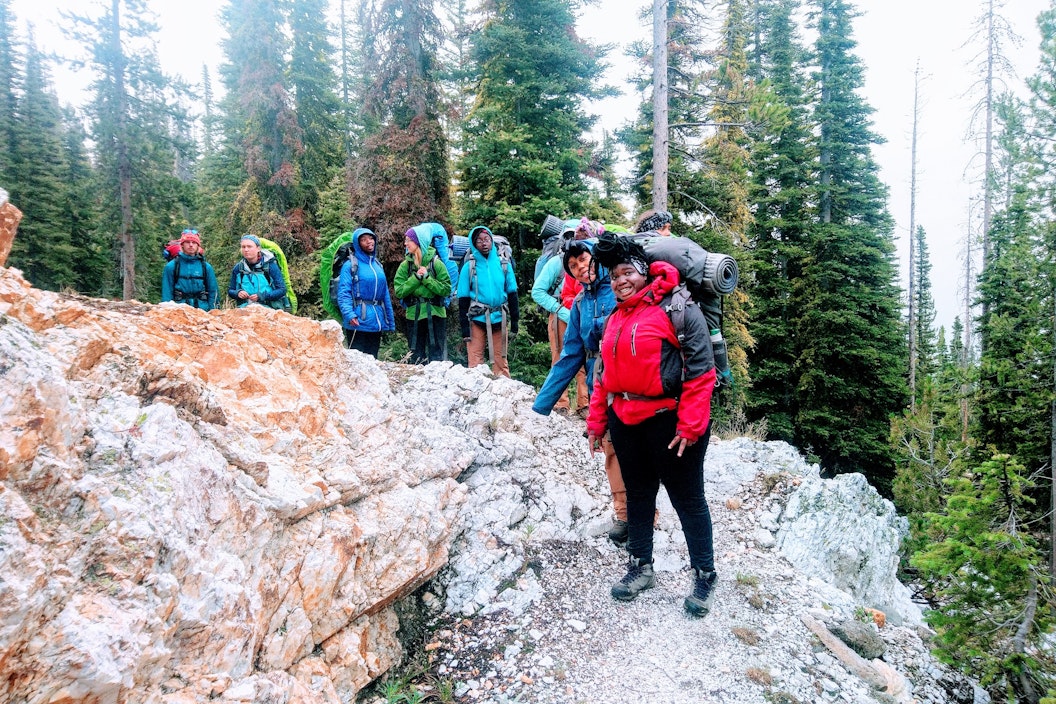 A group of people, all wearing hiking gear and sporting backpacks, smile for a picture on a hike
