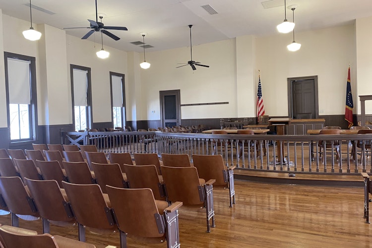 Interior of courthouse, with wooden chairs, bolted to the ground and facing an elevated platform
