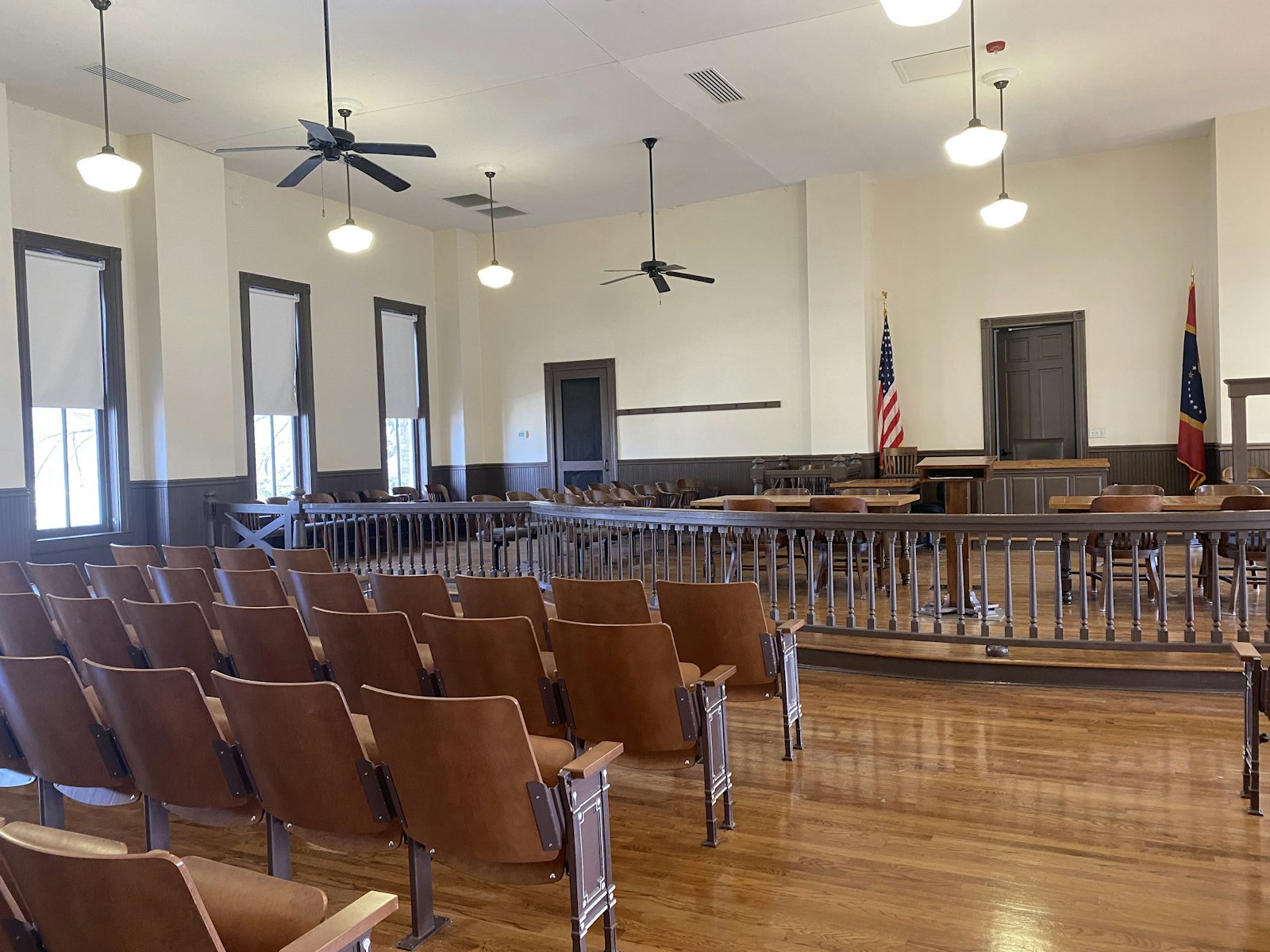 Interior of courthouse, with wooden chairs, bolted to the ground and facing an elevated platform