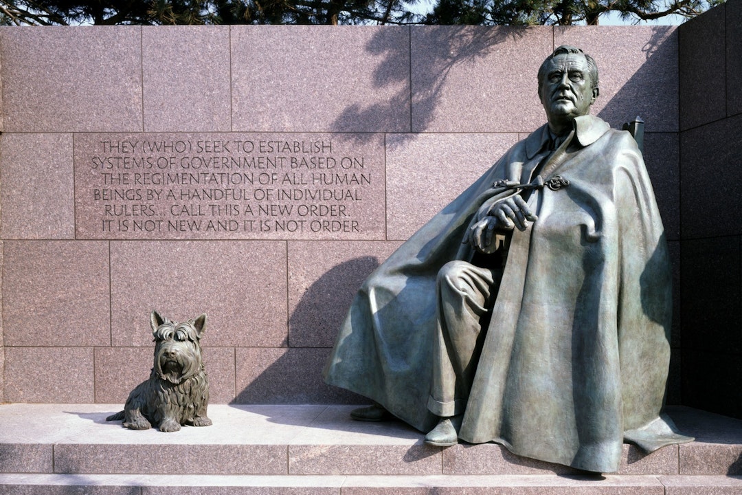Bronze sculpture of FDR, seated and wearing a cloak, next to a small dog