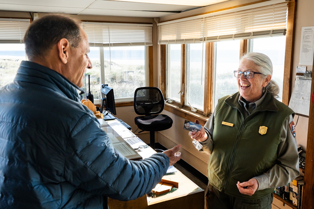 A visitor holds out their hand to receive a pass from a park ranger. They are in a visitor center setting.