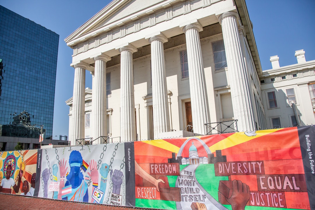On a fence outside a neoclassical courthouse are a set of colorful murals